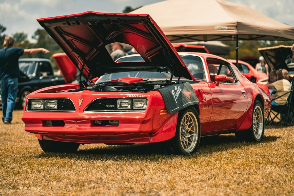 Vintage red Pontiac Trans Am with hood open on display at an outdoor car show.