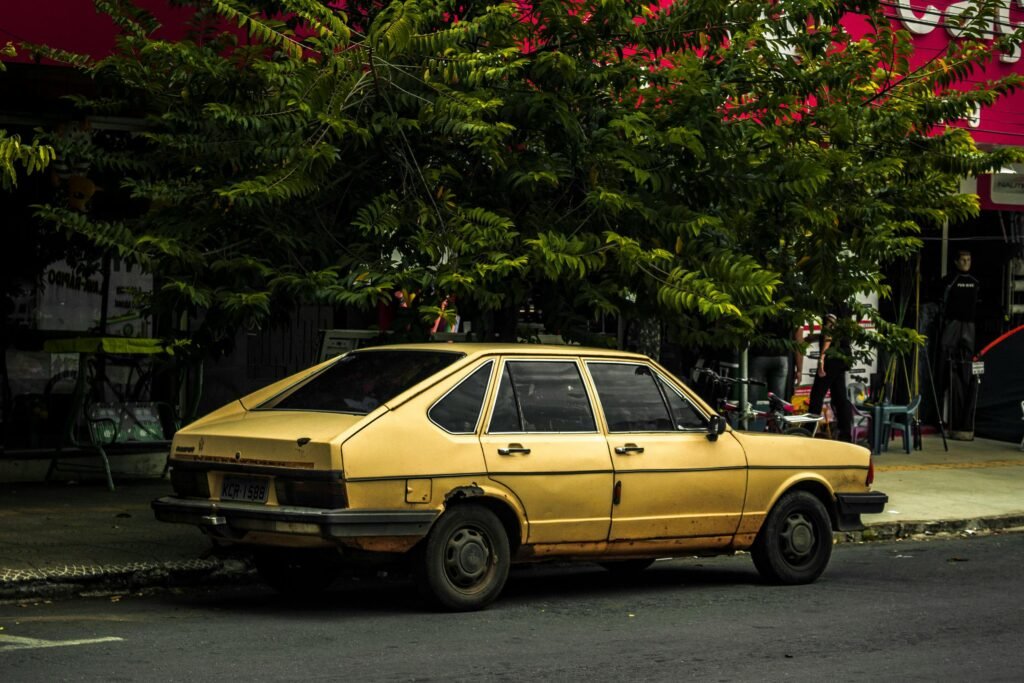 A vintage yellow car parked under a tree on a street in Goiânia, Brazil.